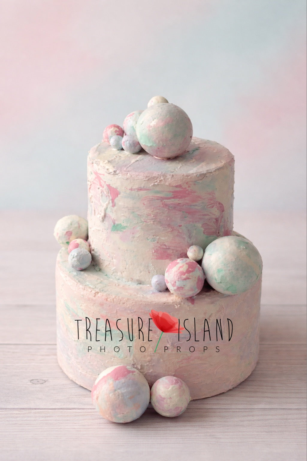 Two-tier faux cake prop for cake smash photography, hand-painted pastel texture in pink and mint tones, decorative spheres, studio background
