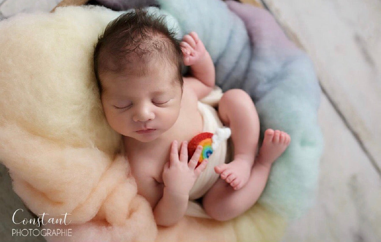 Close-up of a newborn holding a miniature wool felted rainbow and cloud photography prop