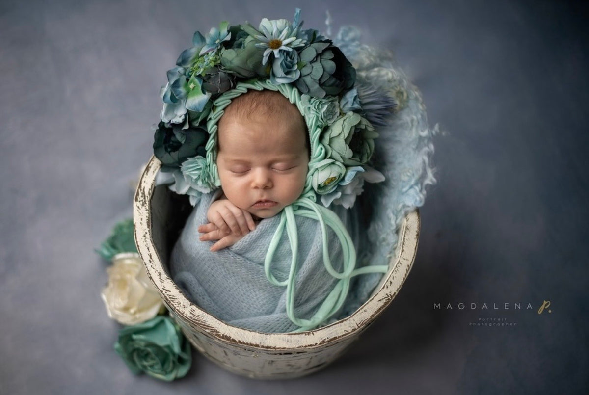 Newborn wearing petrol and mint floral bonnet in a fine art photography setup