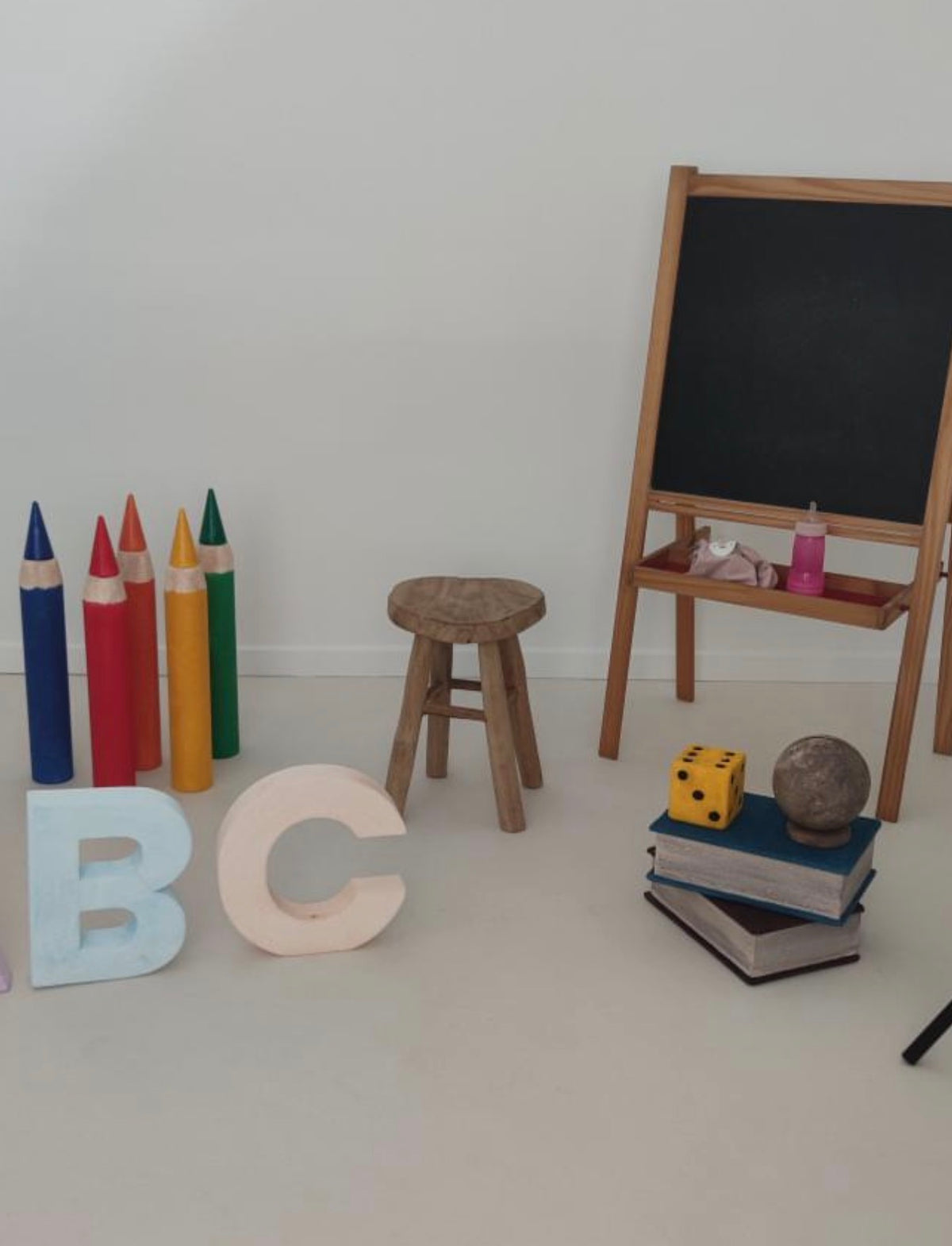 Back-to-school photography scene in a client's studio featuring giant styrofoam crayons, pastel ABC letters, stacked books, a dice and a globe