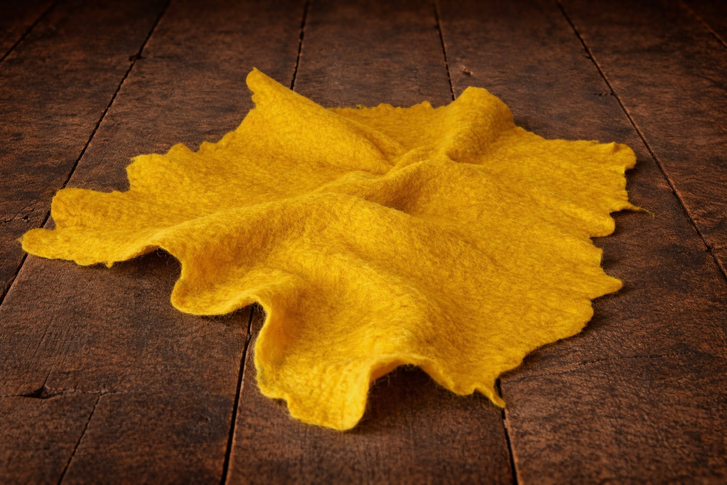 Hand-felted newborn photography wrap in yellow , rolled wool fabric photo prop on dark rustic wooden floor, soft organic texture