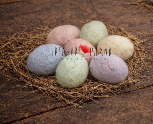 Pastel felted Easter eggs arranged on natural straw nests on rustic wooden floor – newborn photography props
