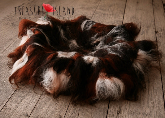 A pile of shaggy, curly animal fur or faux fur in mixed brown, black, white, and rust-red tones, arranged in a circle on a weathered wooden plank surface. A small red flower graphic appears near the top left with the text 'Treasure Island Photos,' which is treated as a watermark/store mark rather than a product brand.