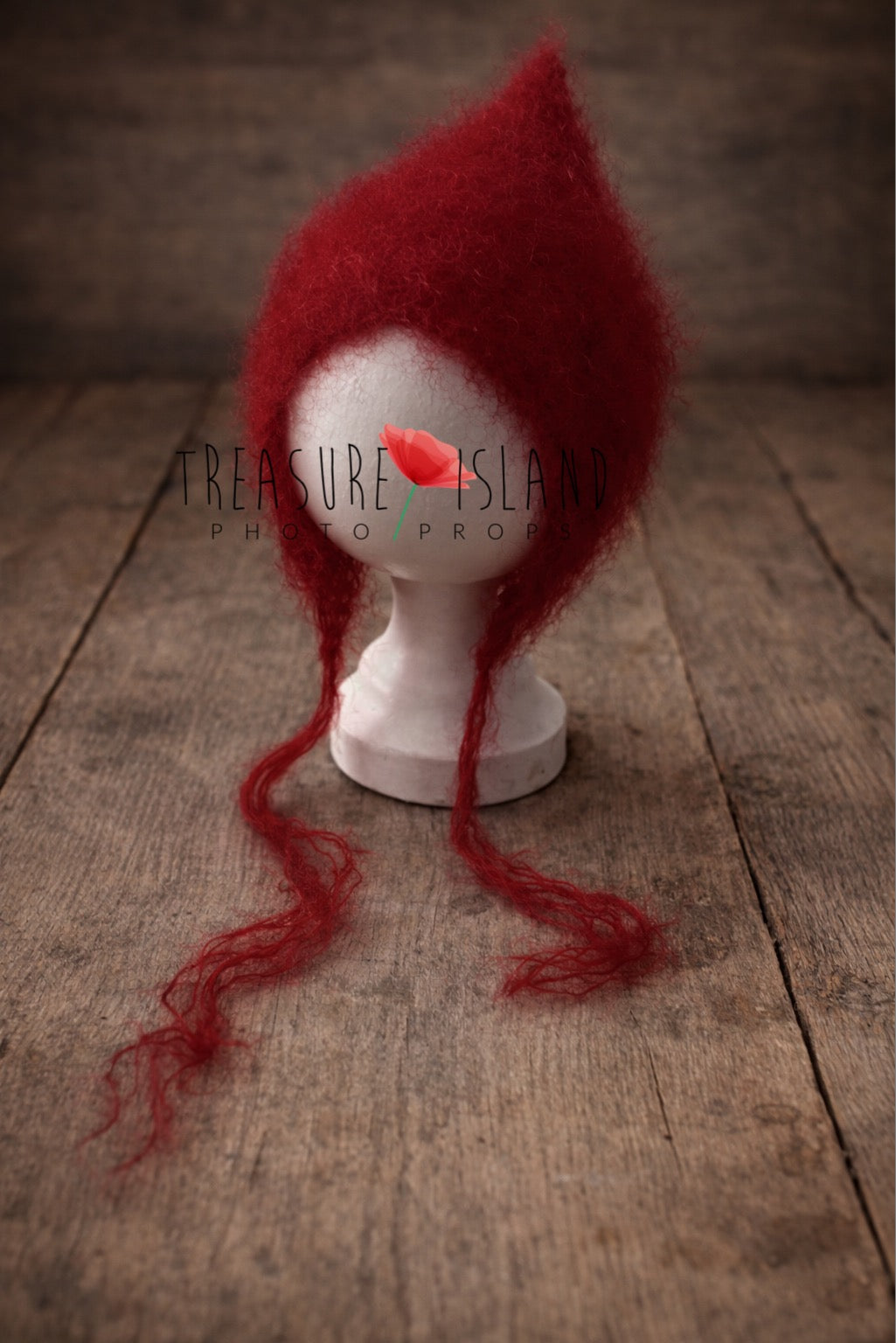 Handmade red newborn pixie bonnet made of soft mohair, displayed on a white mannequin head on a rustic wooden floor background.