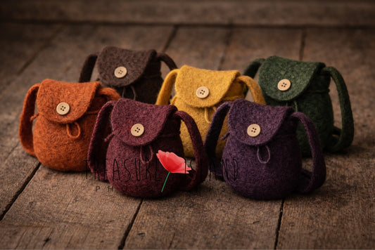 Luxury collection of handcrafted needle-felted miniature backpacks in autumn tones, premium newborn photography props arranged on aged wooden floor