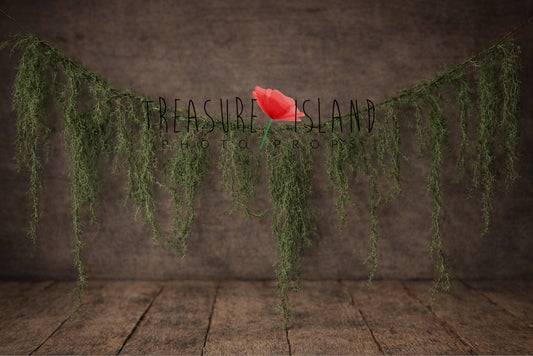 Artificial Spanish moss garland hanging over a rustic wooden floor backdrop, styled for woodland newborn photography setups.

