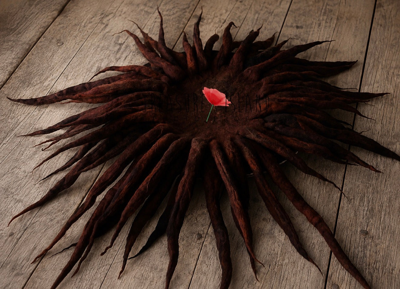 A dark brown dreadlock hairpiece arranged in a circular, sunburst shape on a rustic wooden surface, with a small red flower tucked into the center.