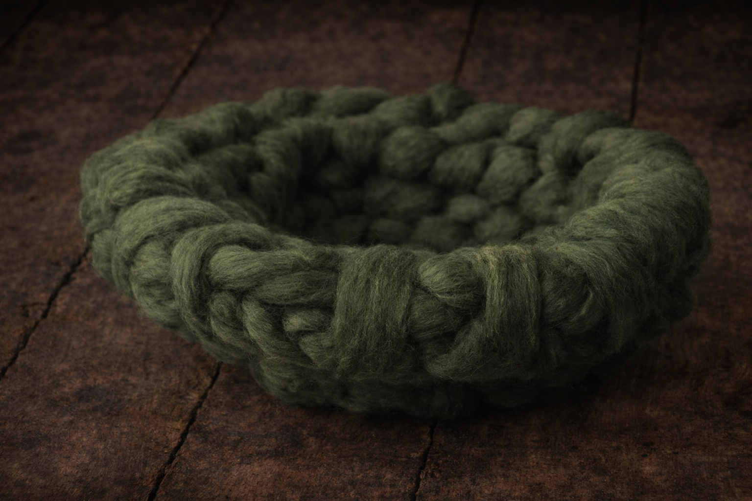 Moss Whisper chunky knitted nest on a dark wooden surface