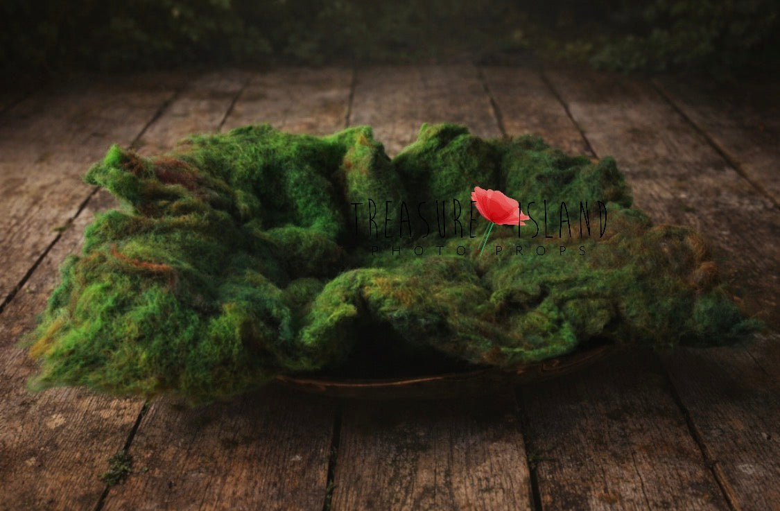 Moss-covered leaf-shaped object with a red flower on a wooden surface