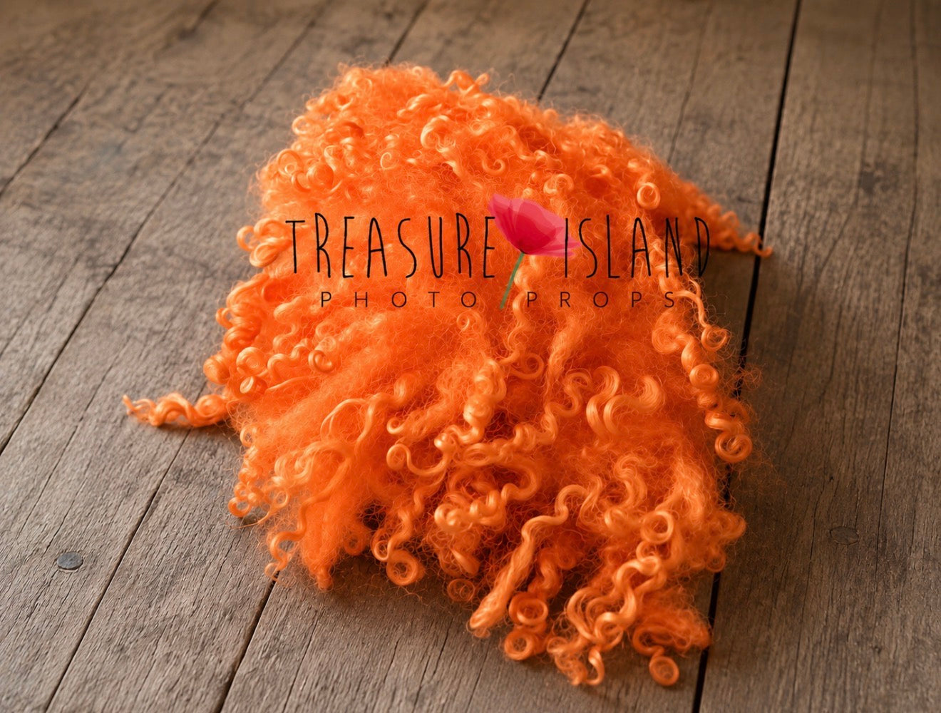 A fluffy, curly orange wig or hairpiece styled on a rustic wooden surface, with a small pink flower tucked into the center. A watermark reading 'Treasure Island Photo Props' is overlaid across the middle.