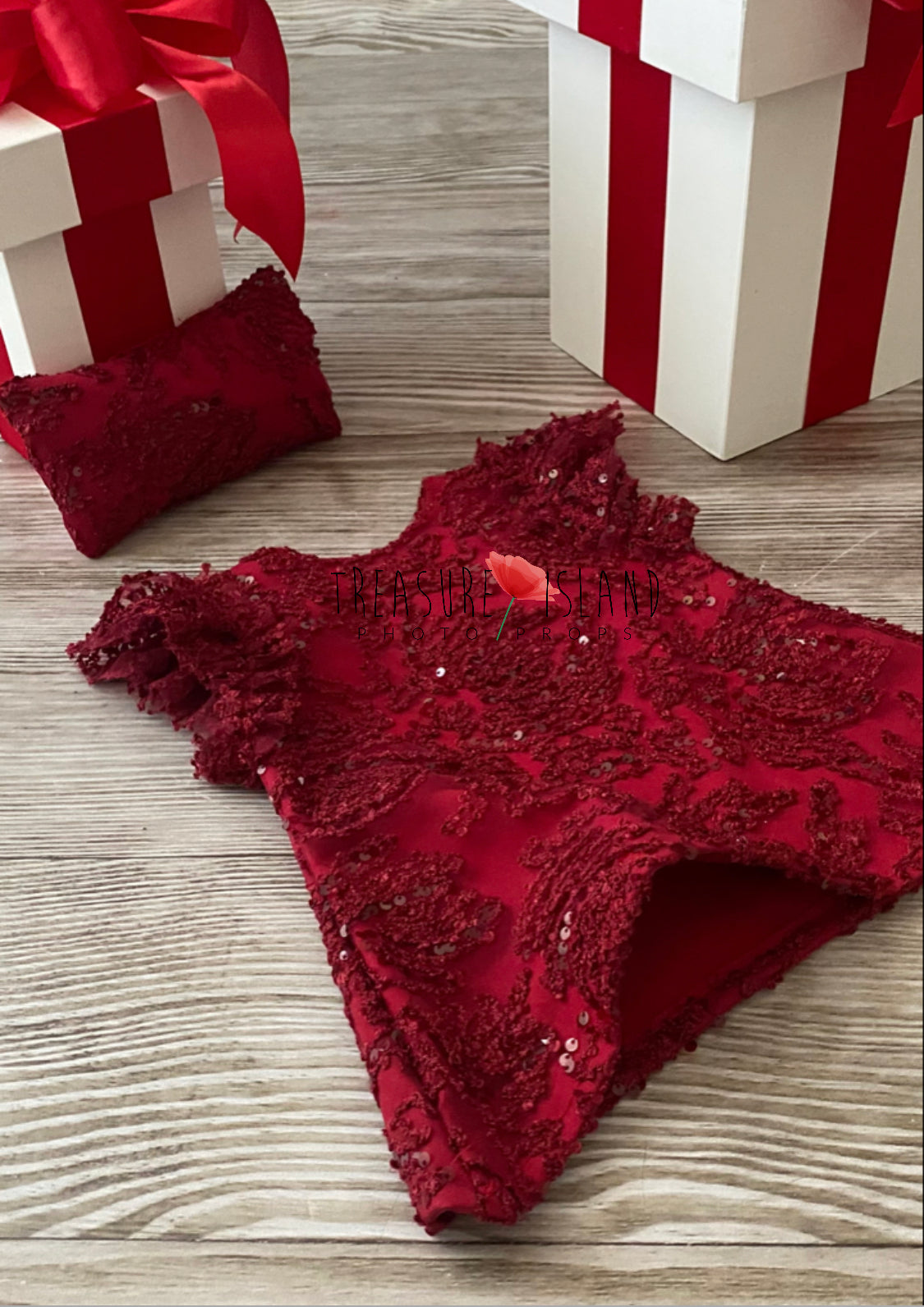 A red luxury dress with silver elements, laid out on a wooden surface next to a white gift box with red ribbon presents.