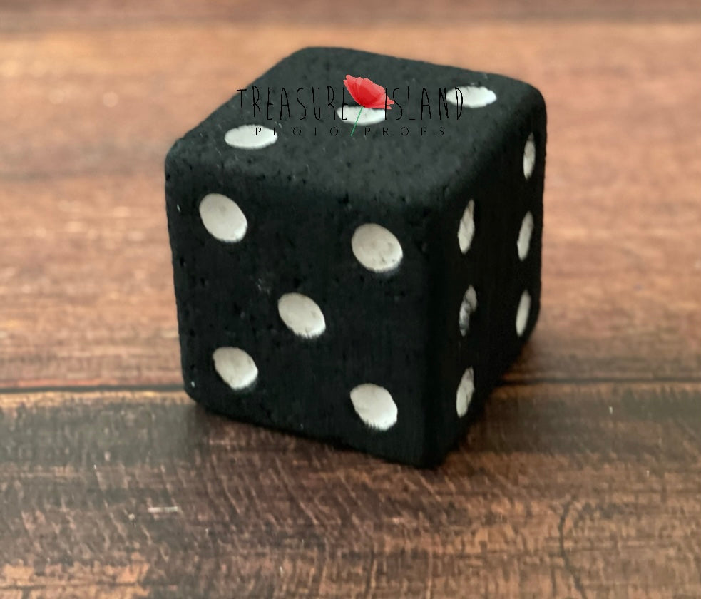 Single handmade black Styrofoam die with white dots and a textured finish, displayed on rustic wooden flooring