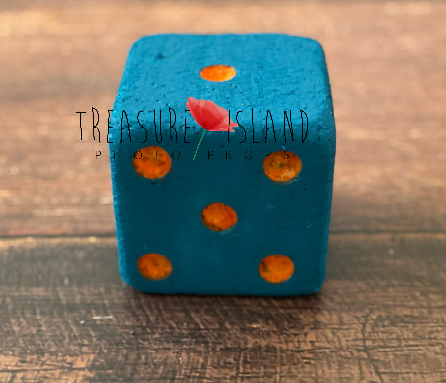 Blue die with orange dots on a wooden surface, branded 'Treasure Island Photo Props'.
