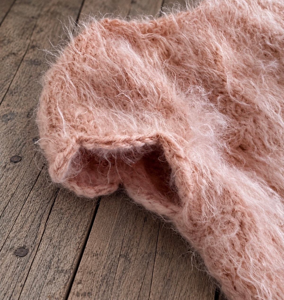 Close-up of the delicate fluffy knit texture and decorative sleeve edge of a dusty pink newborn photography bodysuit.