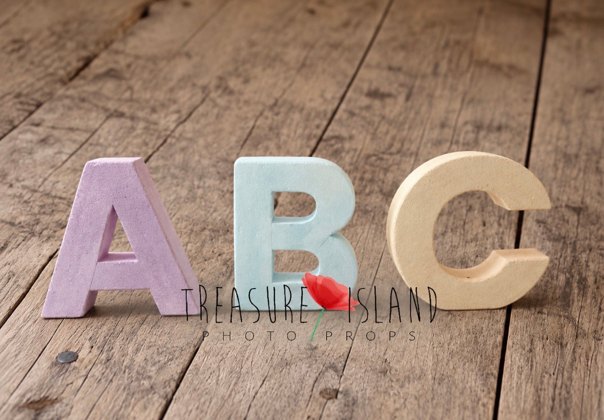Three giant styrofoam ABC letters in lavender, powder blue and vanilla beige, displayed on a rustic wooden floor as photography props