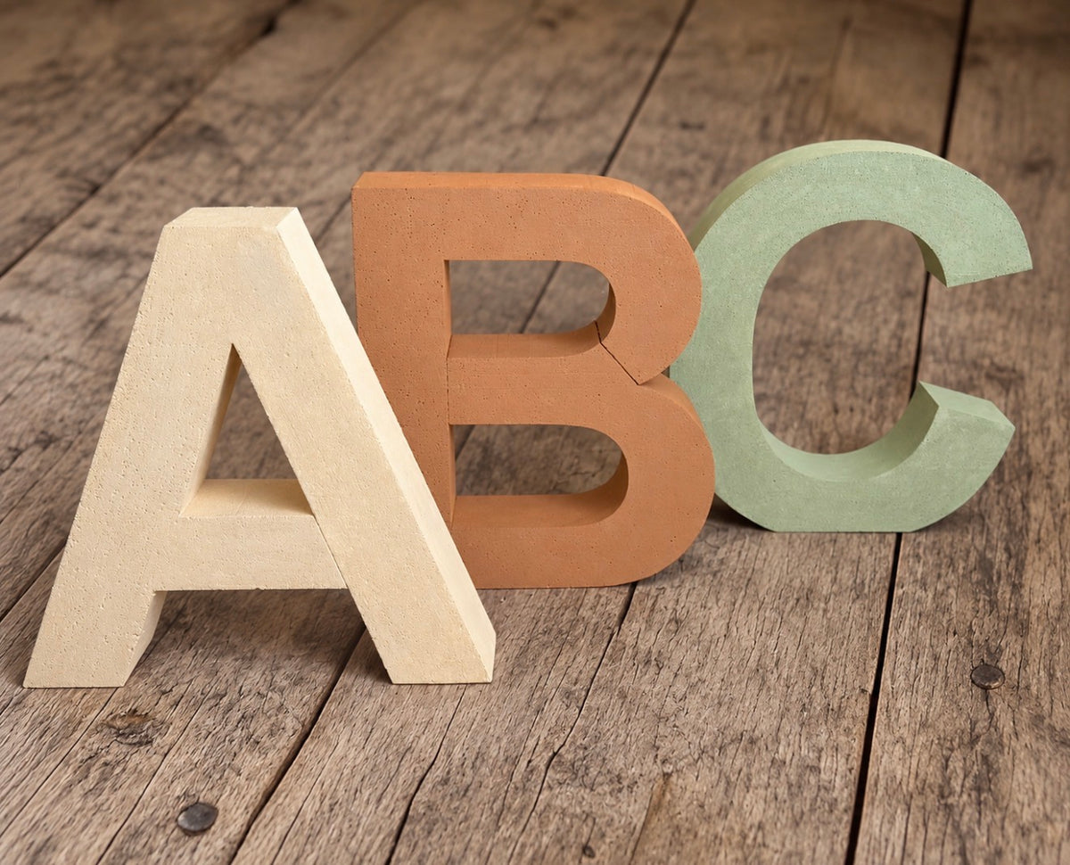 Oversized styrofoam ABC letters in pumpkin cream, terracotta and sage green, arranged on a rustic wooden backdrop for children's photography