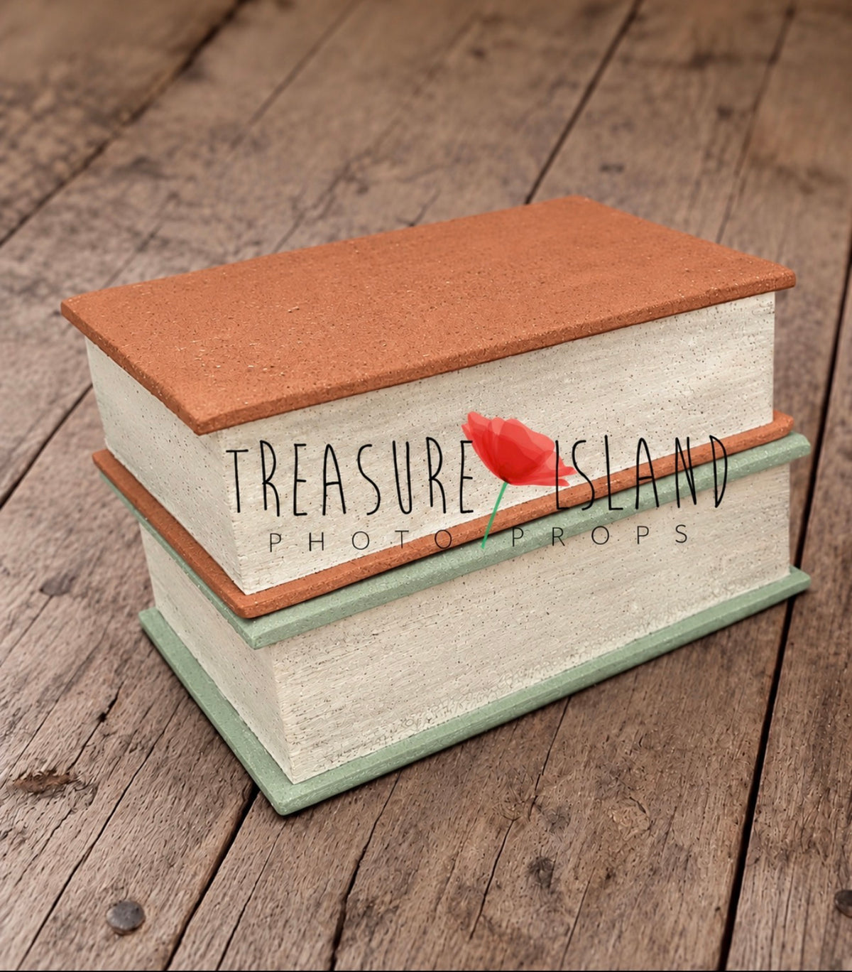Two oversized styrofoam book photography props stacked horizontally, with terracotta and sage green covers and textured ivory pages on a rustic wooden floor
