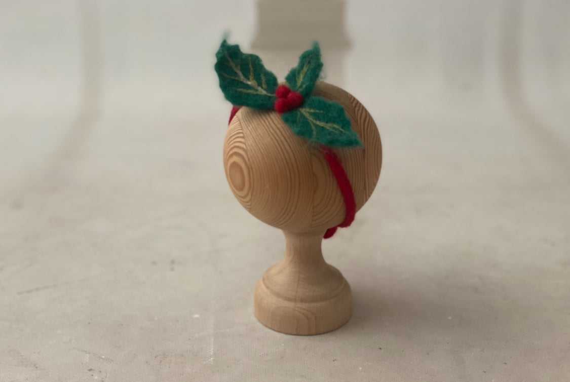 Christmas holly newborn headband with hand-felted green leaves and red berries shown on a photography prop stand