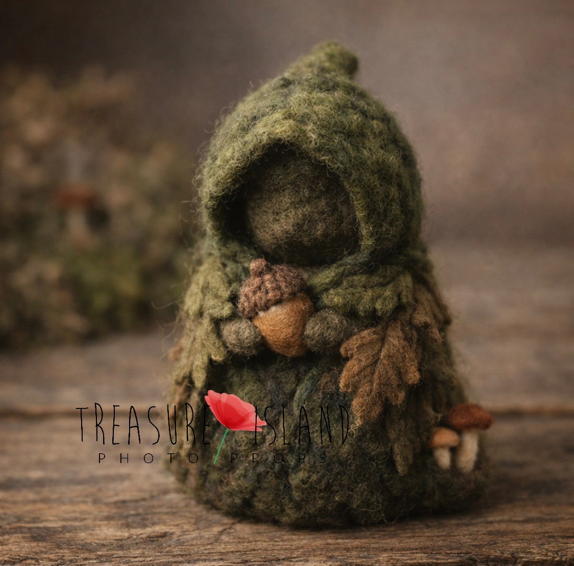 Miniature hand-felted forest guardian figure in a moss green hood holding an acorn, decorated with felted leaves and mushrooms