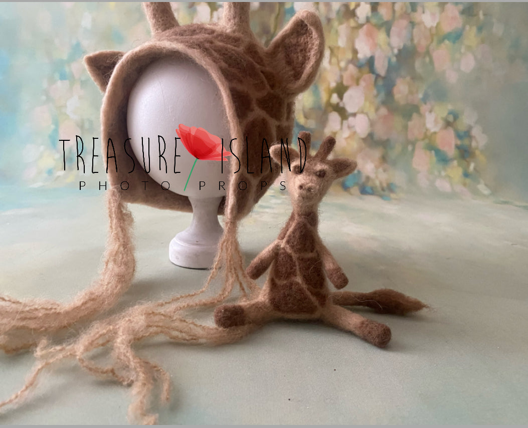 Handmade giraffe bonnet with felted ears and ossicones beside a matching giraffe prop