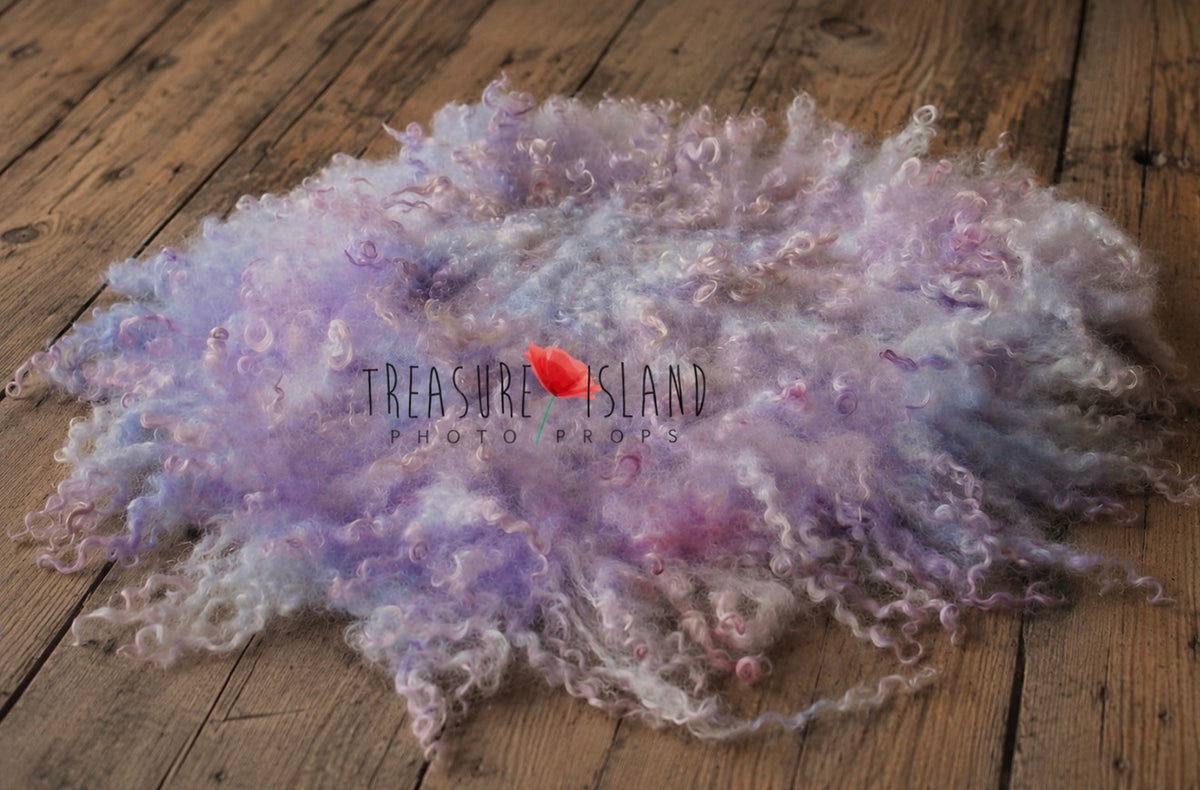 Lilac and lavender hand-felted curly wool blanket spread across rustic wooden floorboards, showing its irregular shape and textured sheep curls