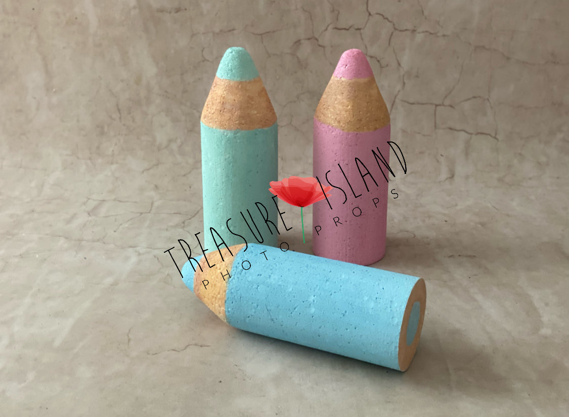 Three handmade mini Styrofoam coloured pencils in turquoise, pink and light blue, with two standing upright and one lying horizontally against a neutral textured background.