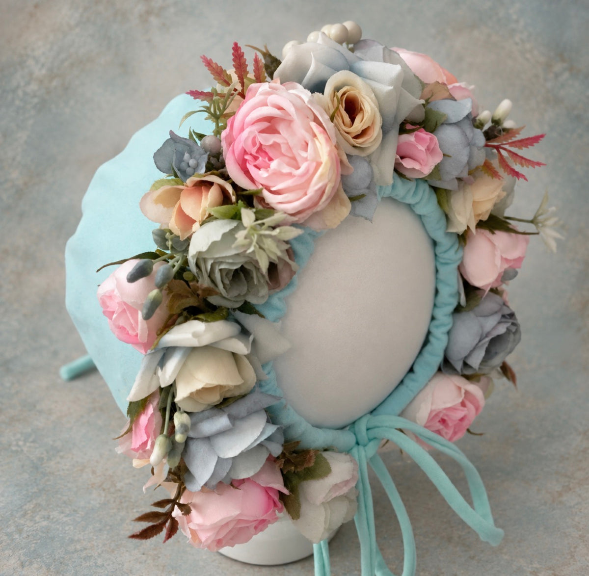 Side view of pastel aqua floral bonnet decorated with blush pink, blue-grey and ivory artificial flowers