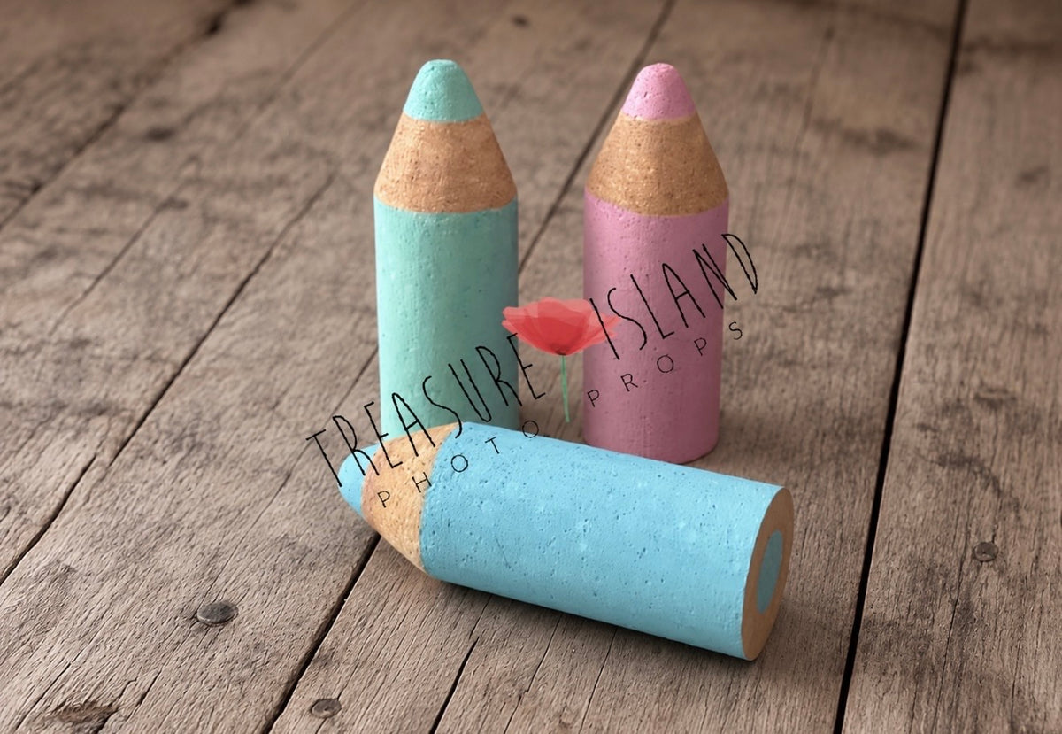 Three pastel Styrofoam pencil props in turquoise, pink and sky blue, arranged on rustic wooden flooring for Back to School photography