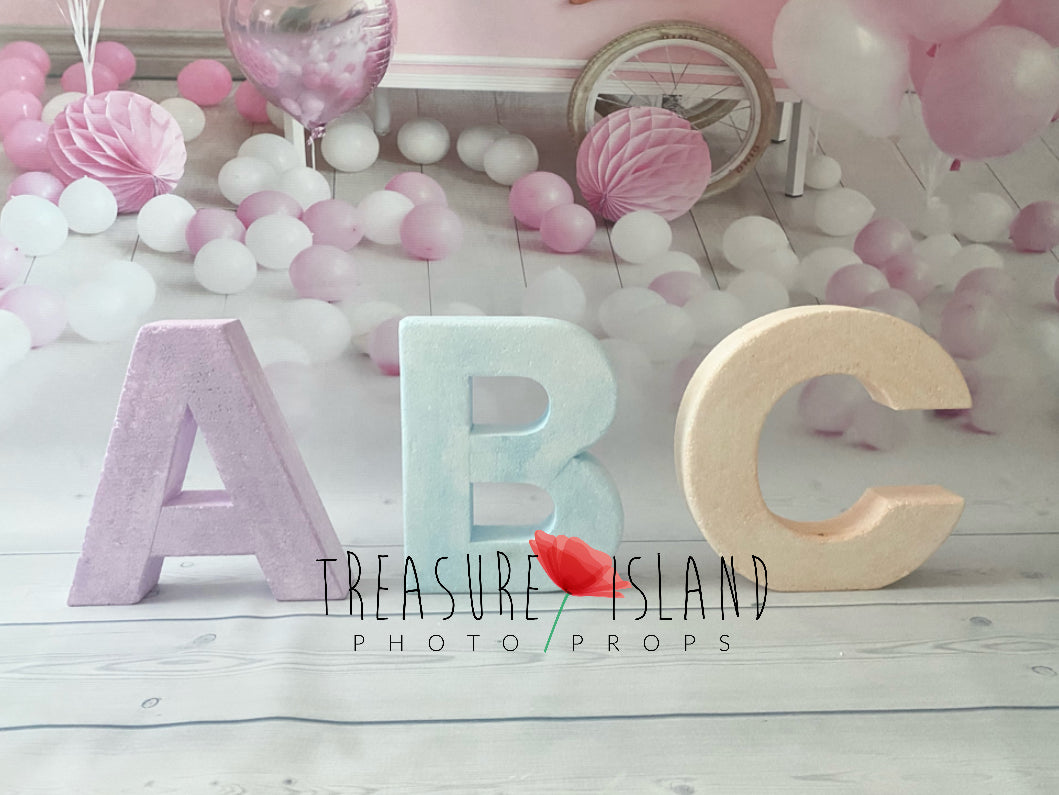 Oversized pastel styrofoam ABC letters arranged in front of pink and white balloons for a children's photography setup.