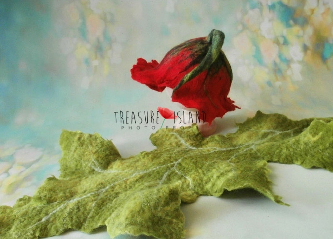 Hand-felted red poppy bonnet displayed with large green veined leaf for newborn photography styling