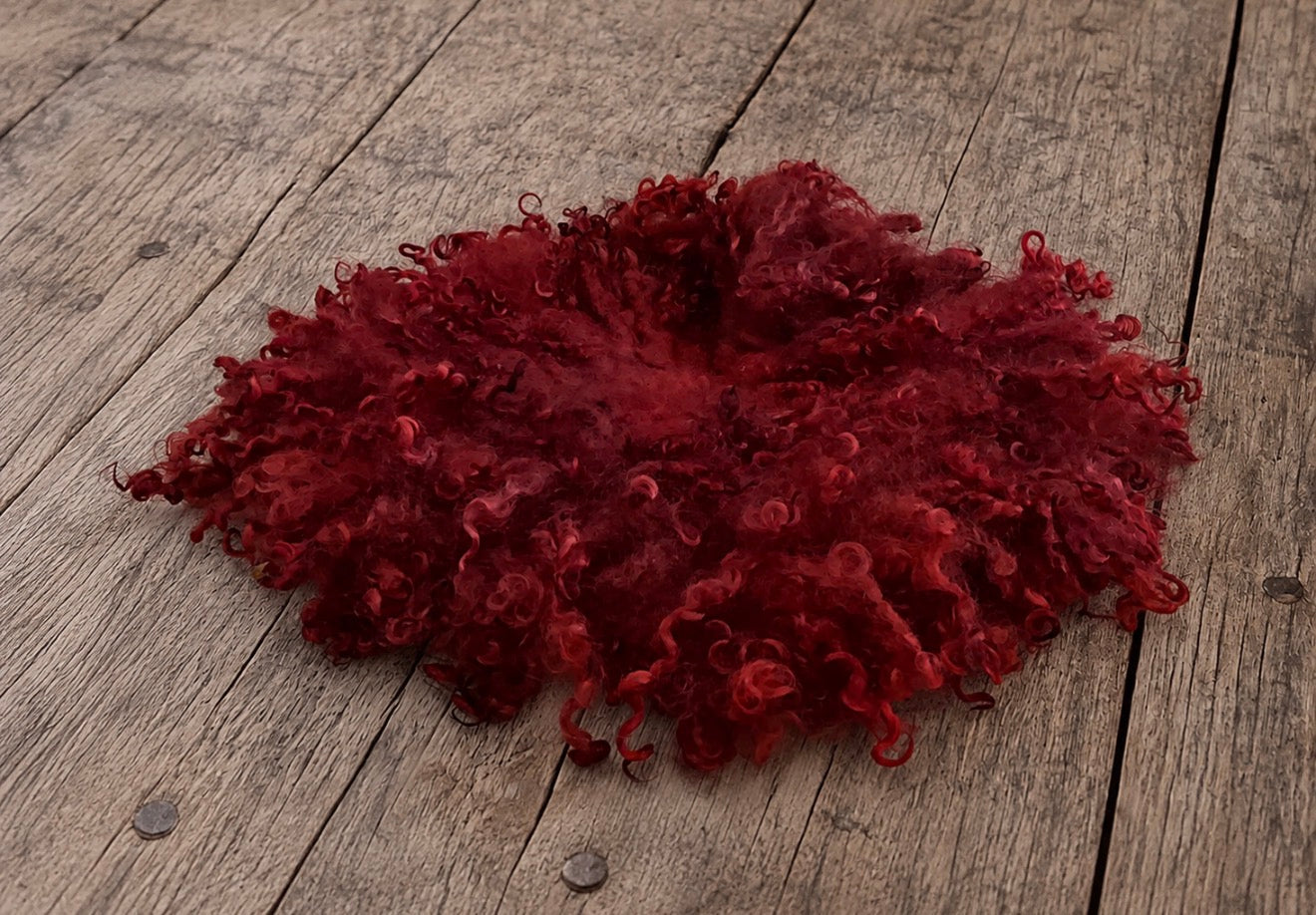 Red curly wool newborn photography blanket displayed on a rustic wooden floor