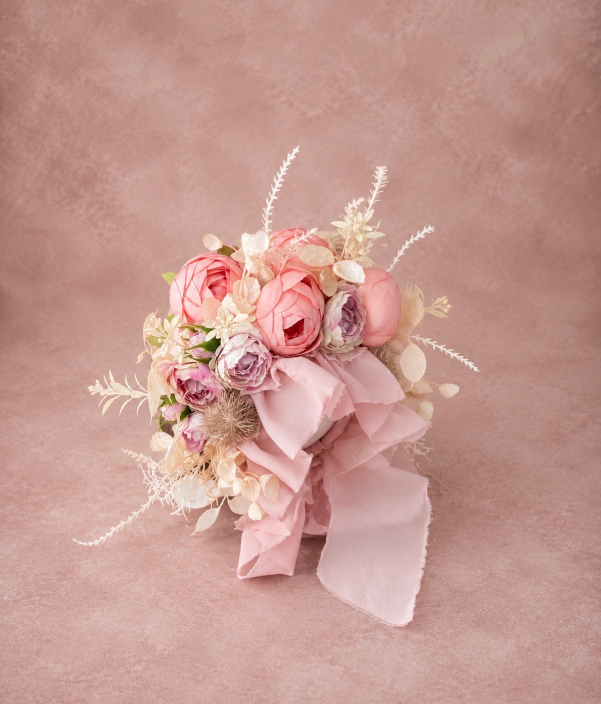 Side view of romantic coral flower bonnet showing layered blooms, foliage and blush ribbons