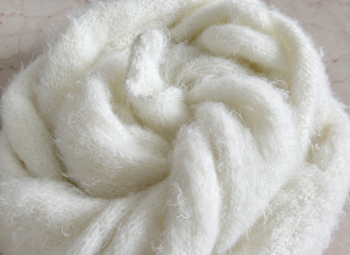 Close-up of a white fluffy long-haired knitted photography wrap, revealing fine fuzzy fibres, delicate knit stitches and soft folds