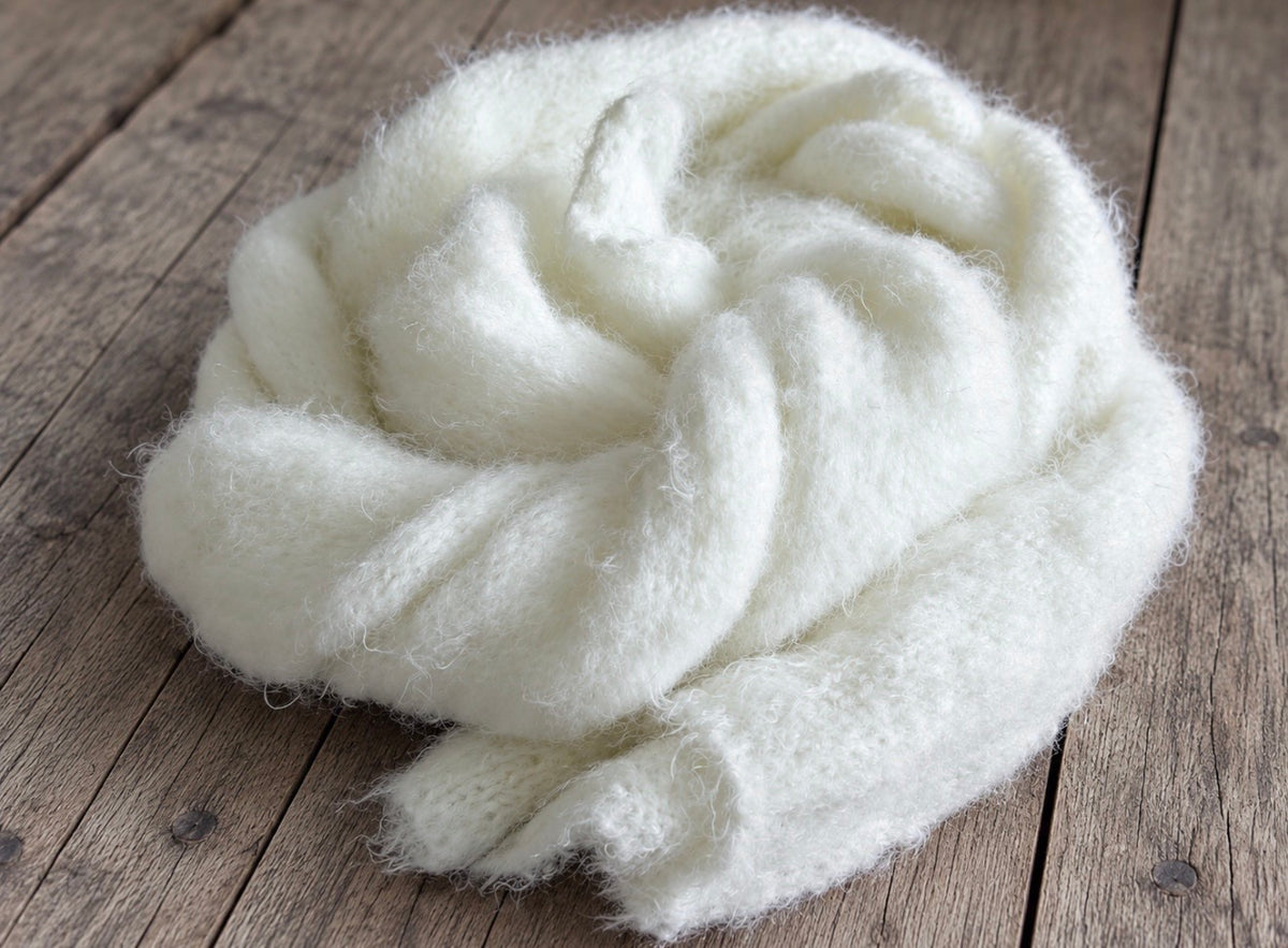 White long-haired knitted newborn photography wrap loosely gathered into a rounded shape, highlighting its fluffy volume and soft, layered folds
