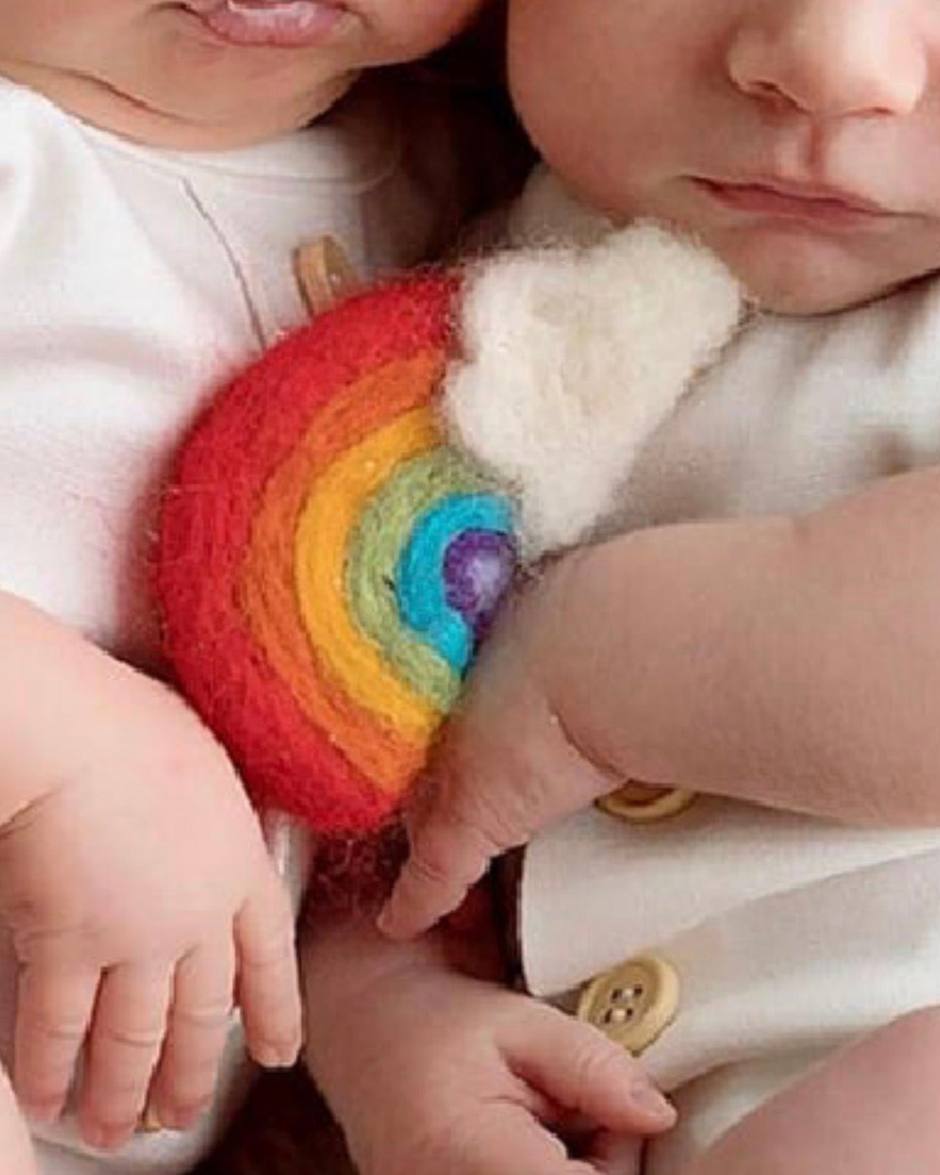 Small handmade wool rainbow and cloud held in a newborn baby's hand