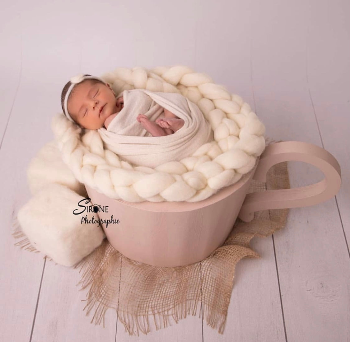 Hand-knitted wool nest styled inside a wooden cup for a newborn photography setup