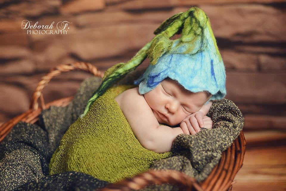 Newborn wearing a blue hand-felted flower hat with long green stalk and leaves
