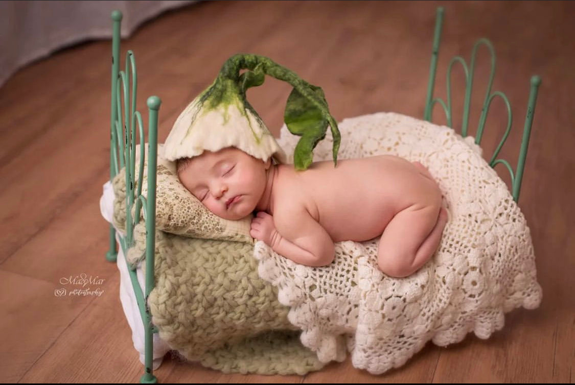 Newborn wearing a white hand-felted flower hat with long green stalk and leaves