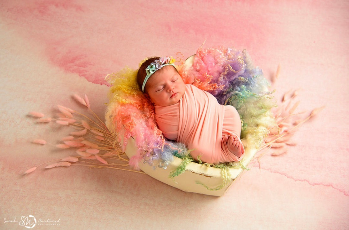 Newborn posed on a pastel rainbow heart-shaped curly wool blanket during a photography session