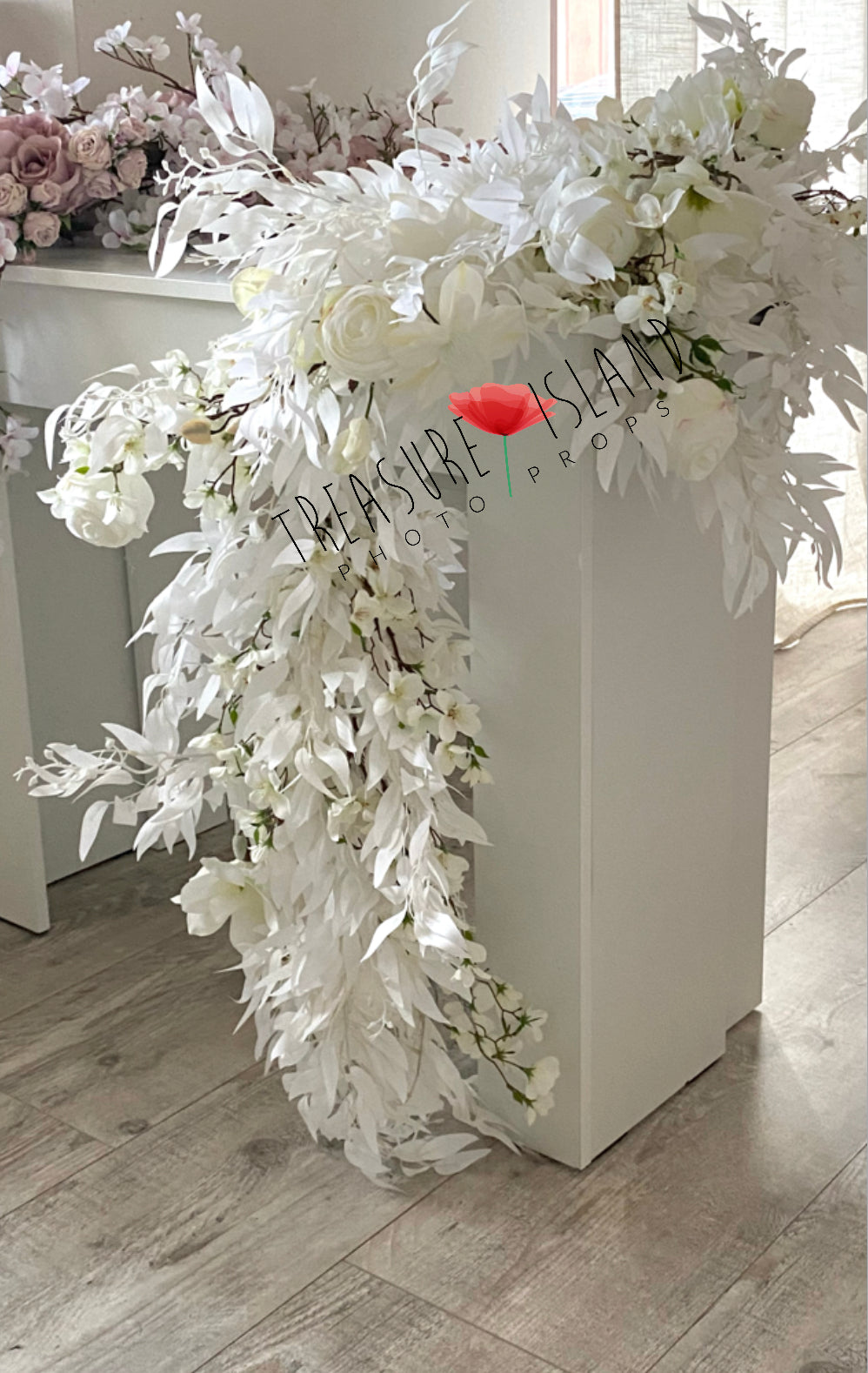 Cascading white artificial flowers and delicate foliage draped over a white studio pedestal, showing an alternative arrangement for photography styling