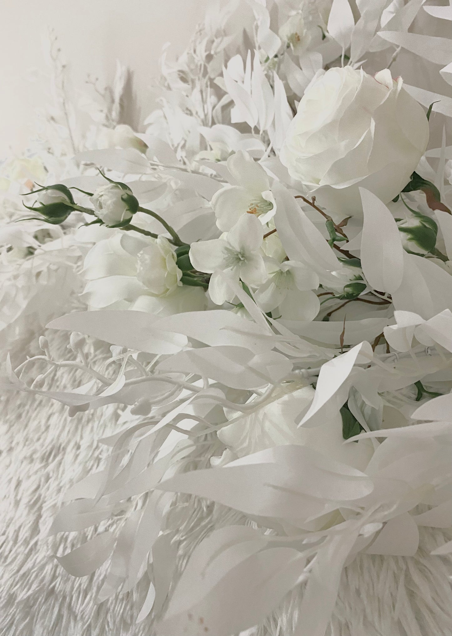 Close-up of white artificial roses, small blossoms and slender cascading leaves showing the layered texture of the floral photography installation